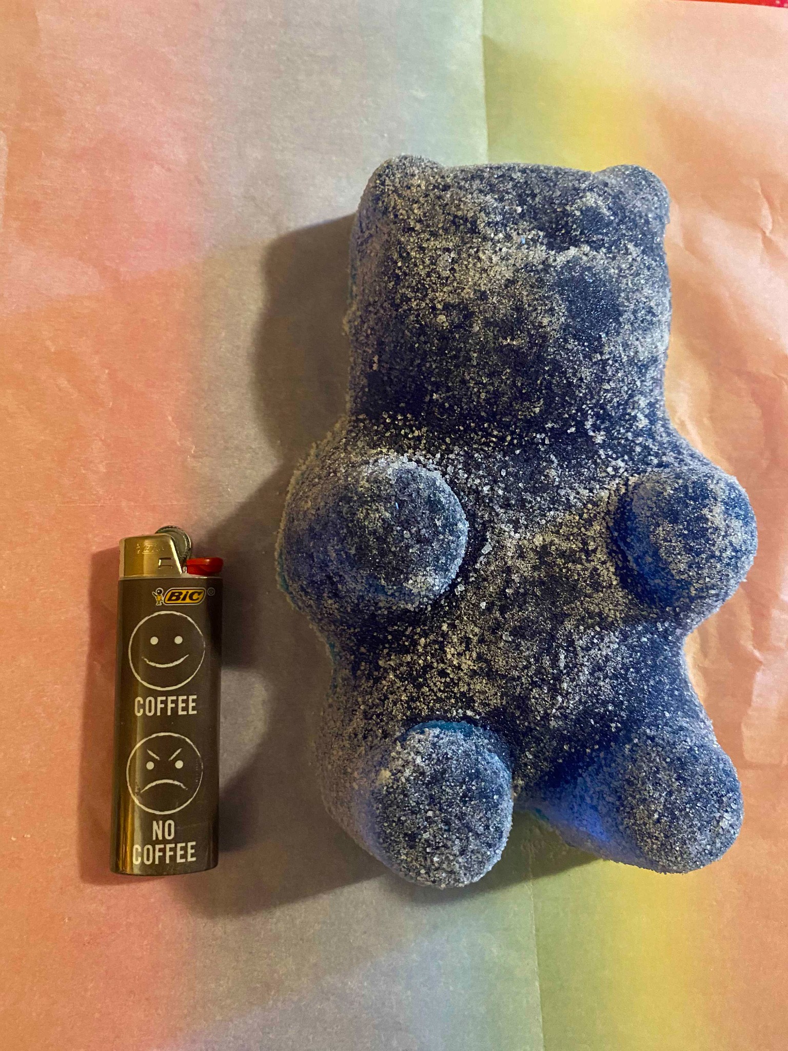 Blue sugar‑coated gummy bear next to lighter on pastel paper